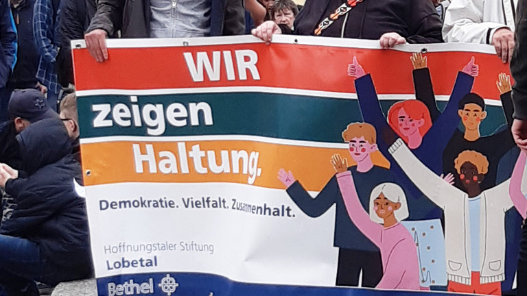 Teilnehmende des Protestmarsches halten ein Banner mit der Aufschrift Wir zeigen Haltung