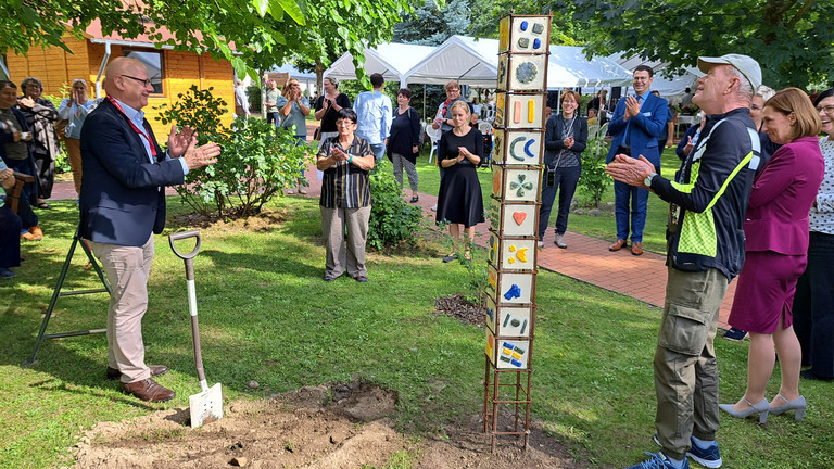 Geschäftsführer Herbert Blum (links) hat für die Nachwelt eine Zeitkapsel bei der von Bewohnenden gestalteten Stele vergraben.